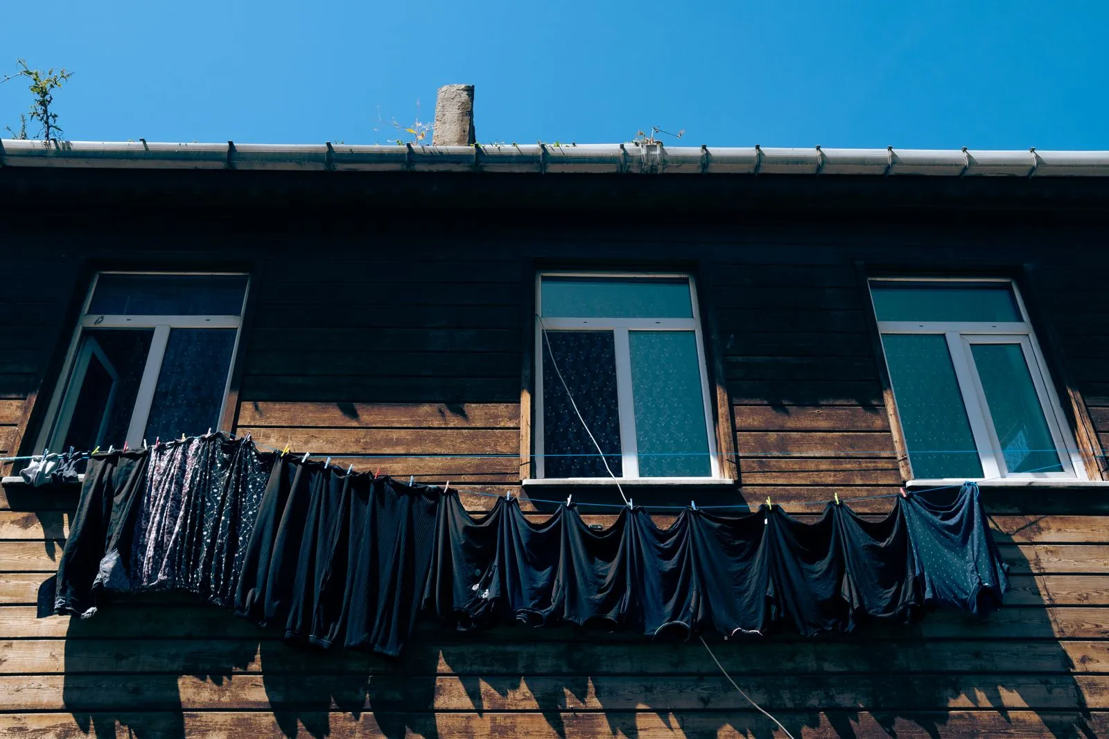 Low angle view of wooden building with laundry drying on clothesline under clear blue sky.